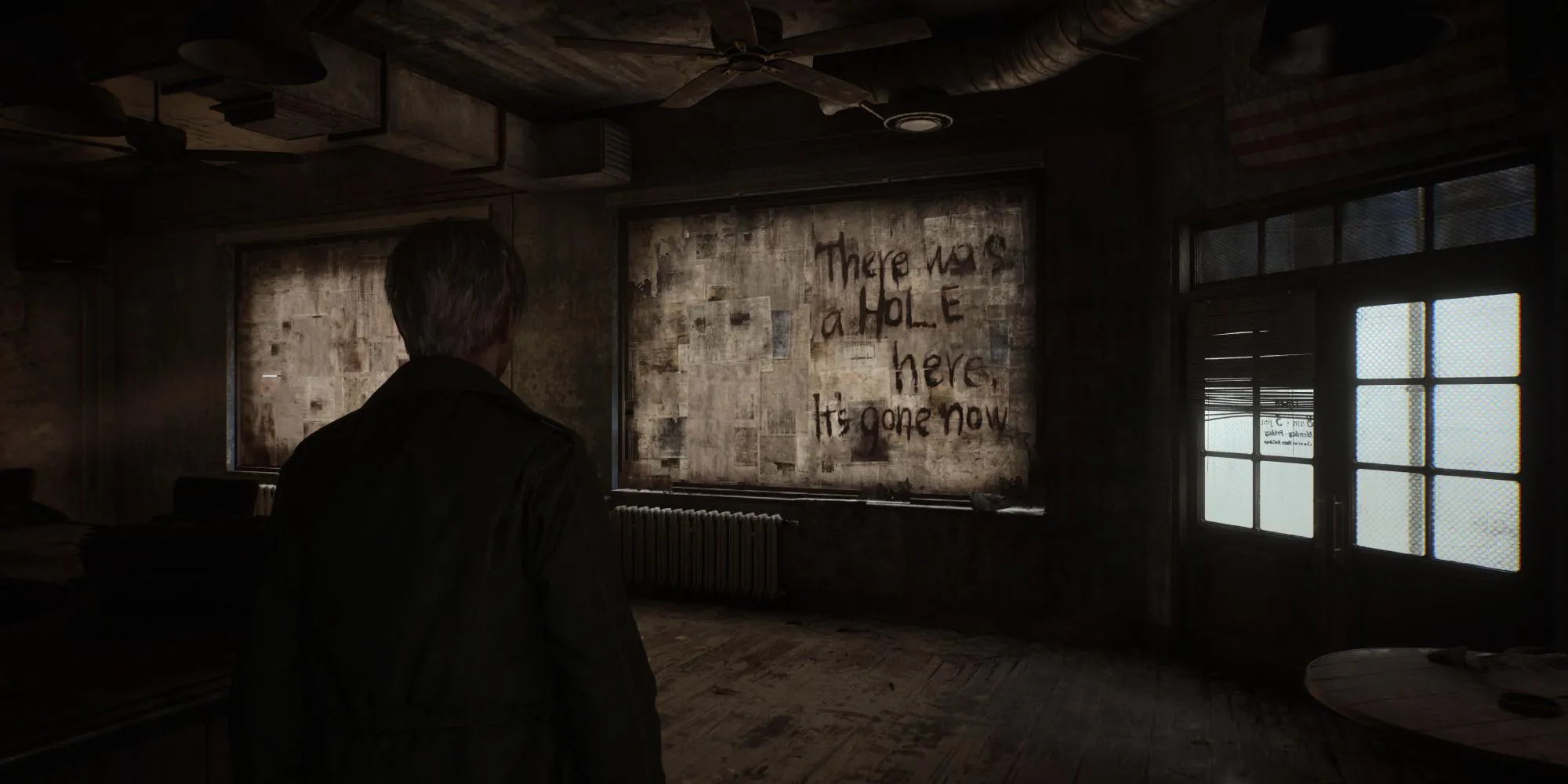 Một cảnh trong Silent Hill 2 Remake với thông điệp bí ẩn trên tường và một lỗ hổng đáng sợ
